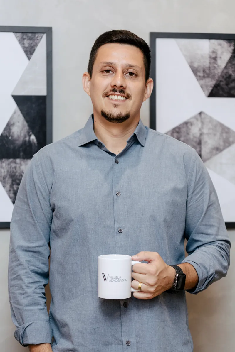 Dr. Felipe Villela Gaspar sorrindo, segurando uma caneca com o logotipo do escritório
